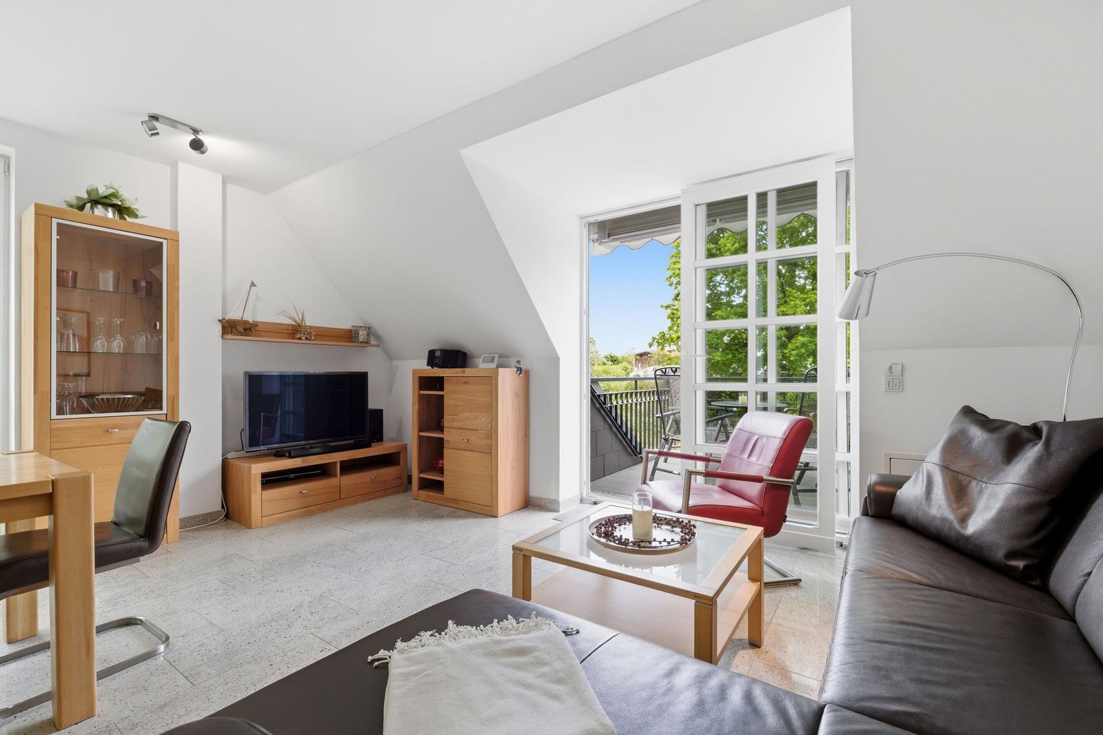 Living room with sofa, TV, and balcony access. Wooden furniture and red leather chairs.