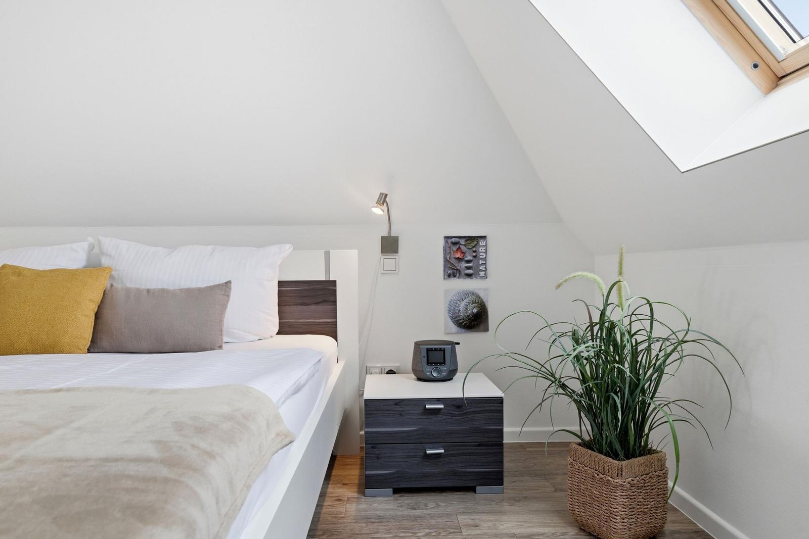 Bedroom with sloped ceiling, bed, nightstand, and plant