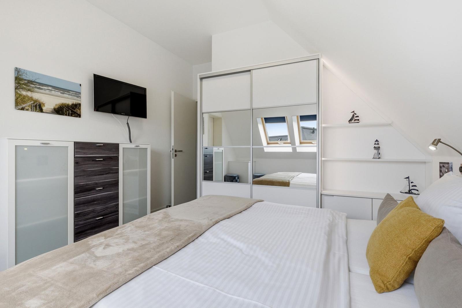 Bedroom with bed, mirrored wardrobe, and TV mounted on the wall.