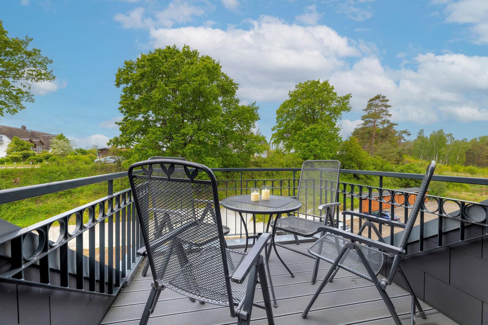 Terrace with table and chairs, view of green trees and blue sky.
