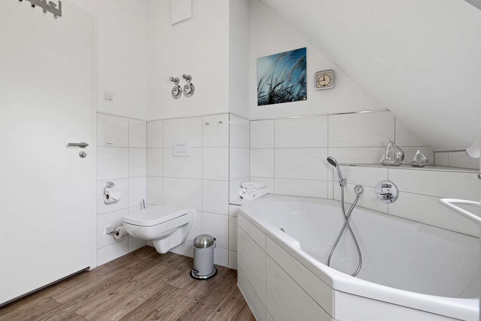 Bathroom with shower, bathtub, and toilet. Wooden floor and white tiles.