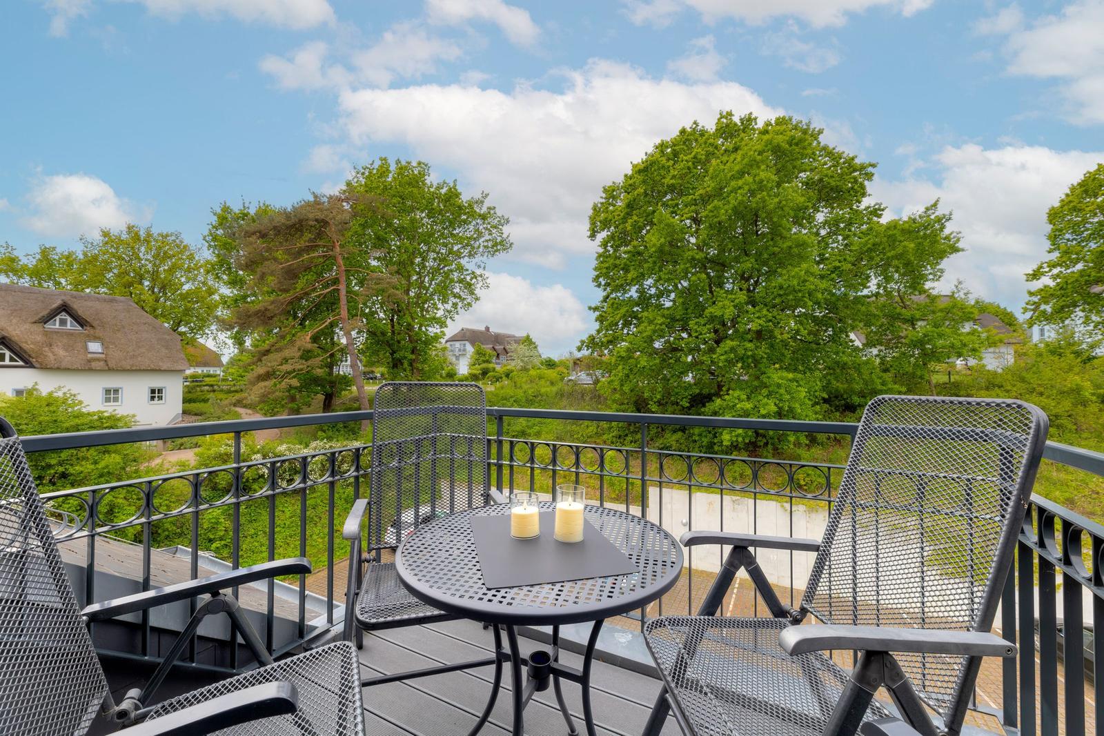 Balcony with table and chairs, view of green trees and houses.