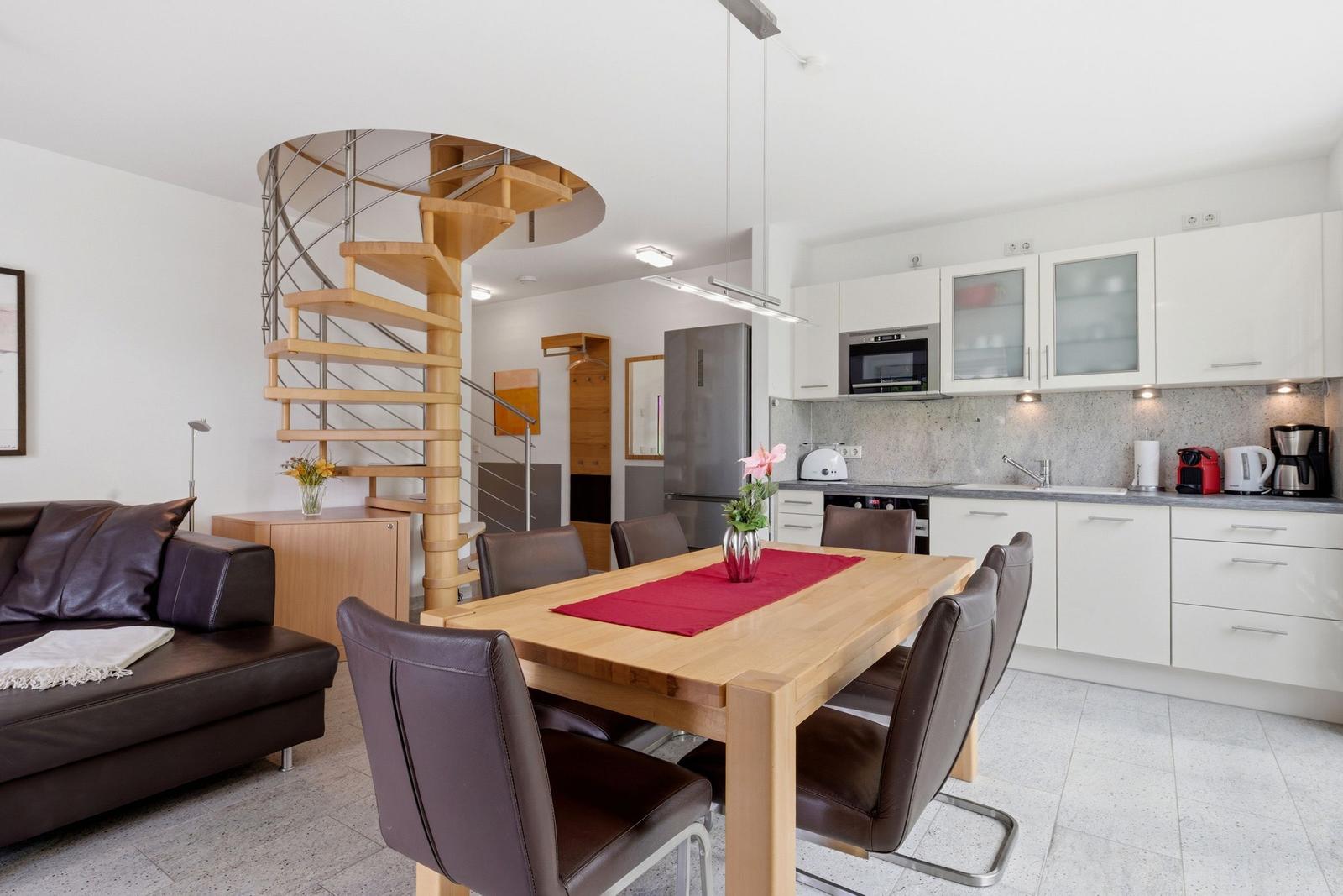 Dining area with wooden table, brown chairs, and kitchen with white cabinets.