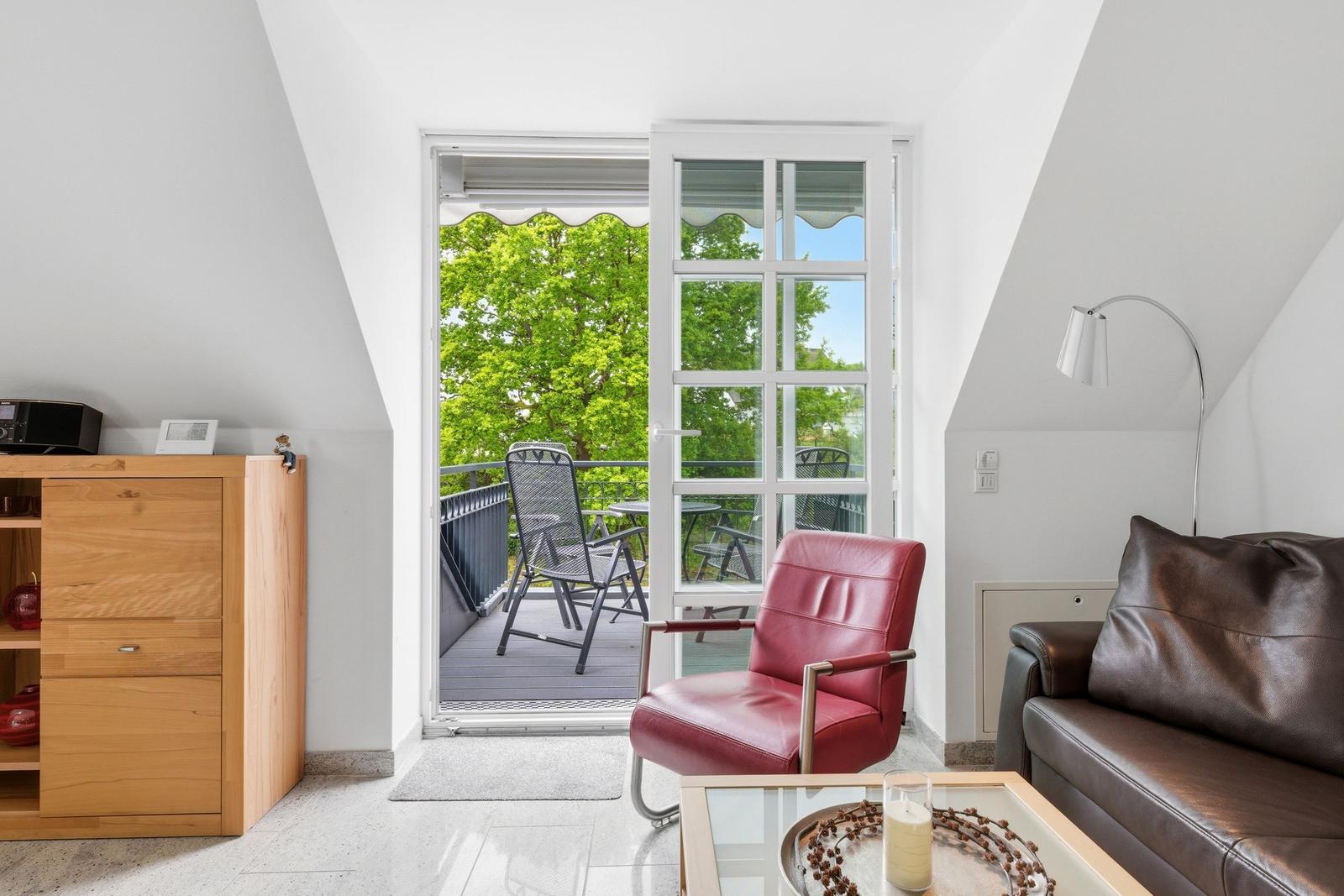 Living room with red armchair, brown sofa, and balcony with table and chairs.