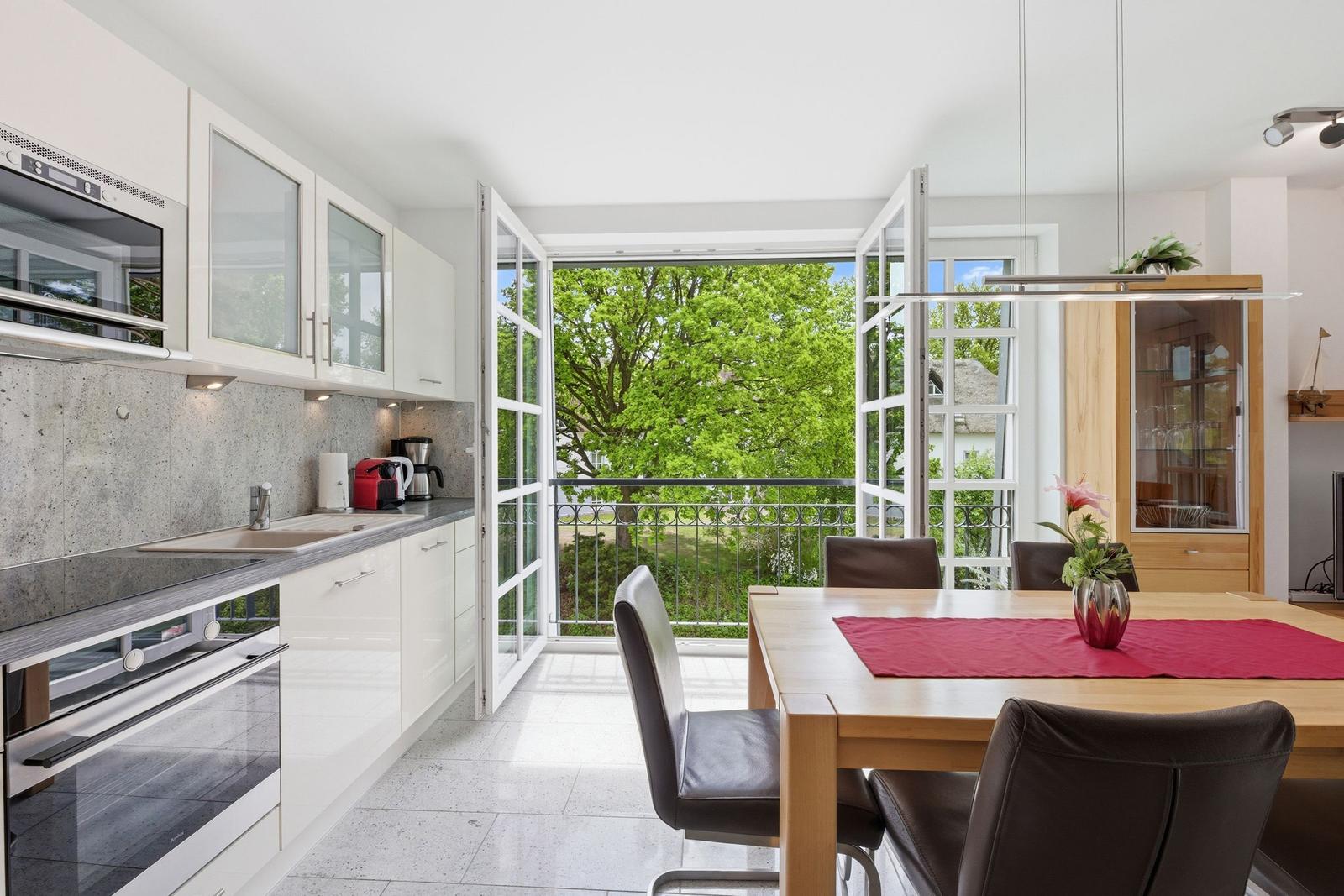 Kitchen with dining area, balcony, and view of green trees.