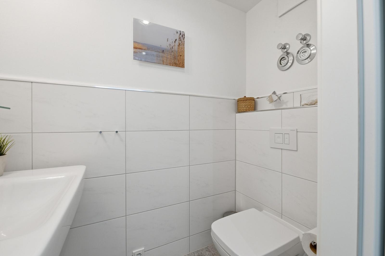 Bathroom with white tiled walls, sink, toilet, and wall picture.