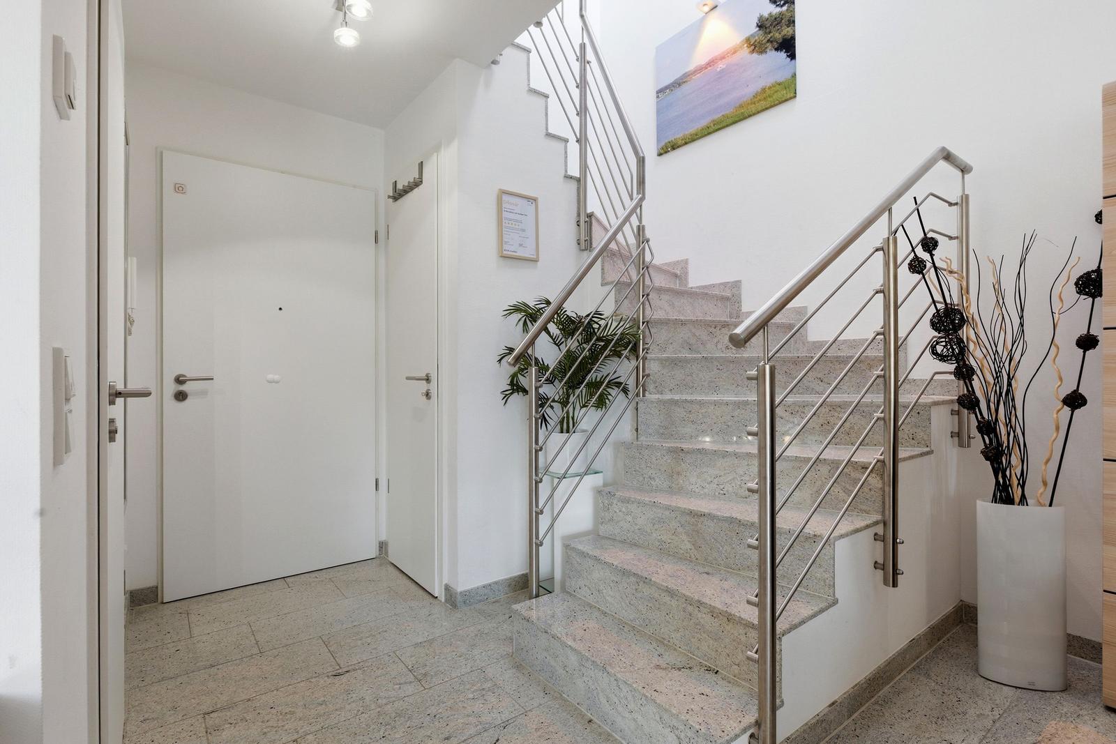 Hallway with stairs, plants, and wall art. White walls and floor tiles.