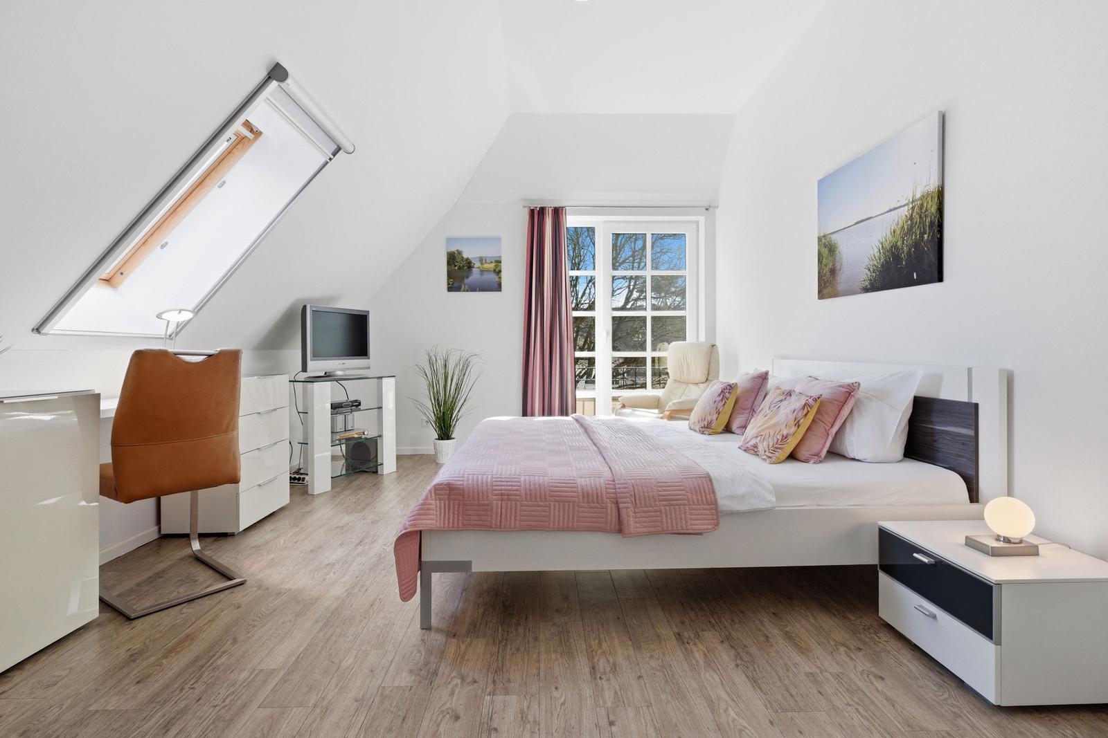 Bedroom with sloped ceiling, bed, desk, and TV.