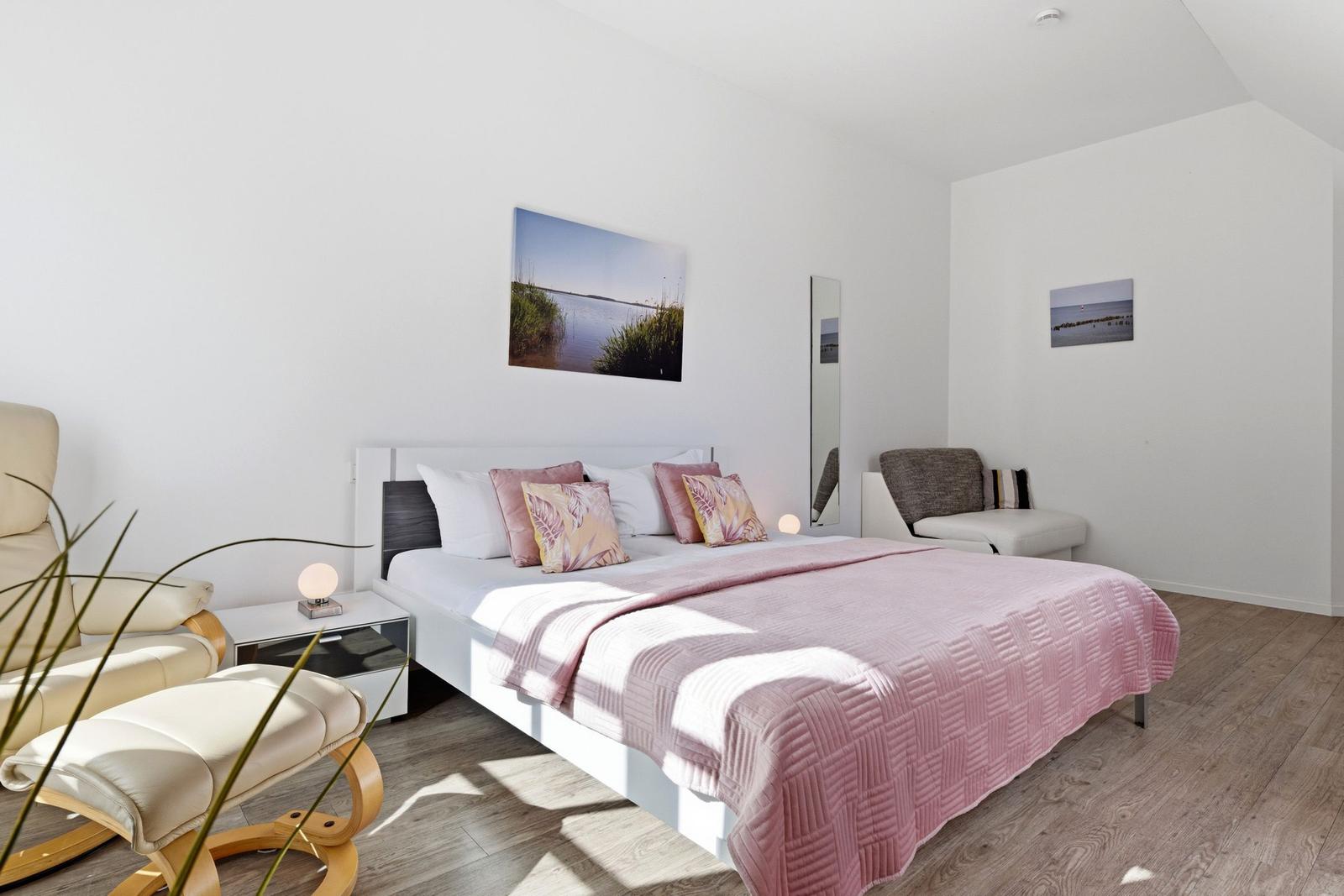 Bedroom with bed, armchairs, and wall art.