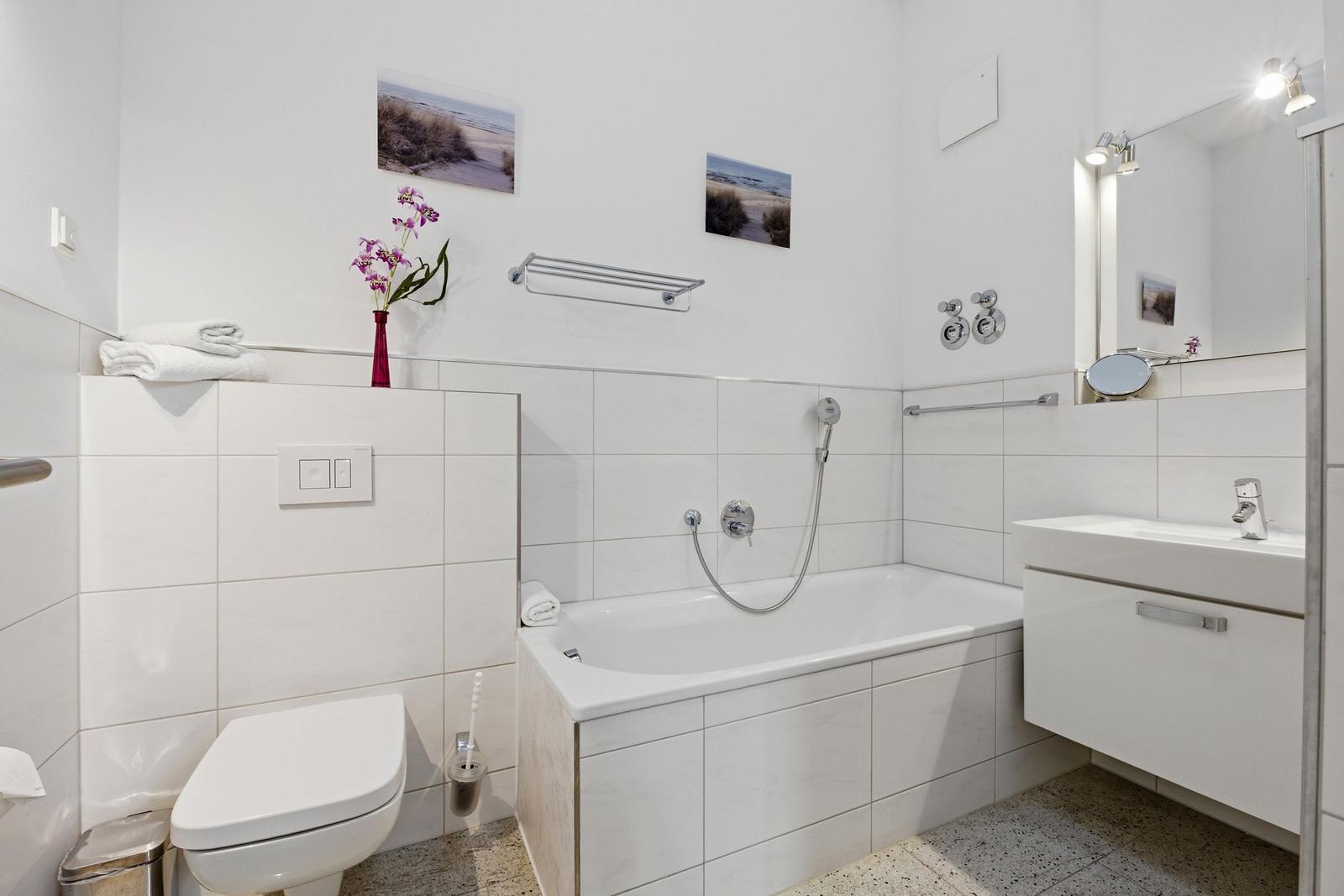 Bath with bathtub, sink, and toilet. White tiles and mirror.
