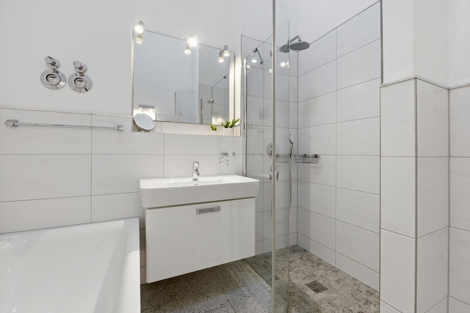 Bathroom with shower, sink and bathtub. White tiles and modern fixtures.
