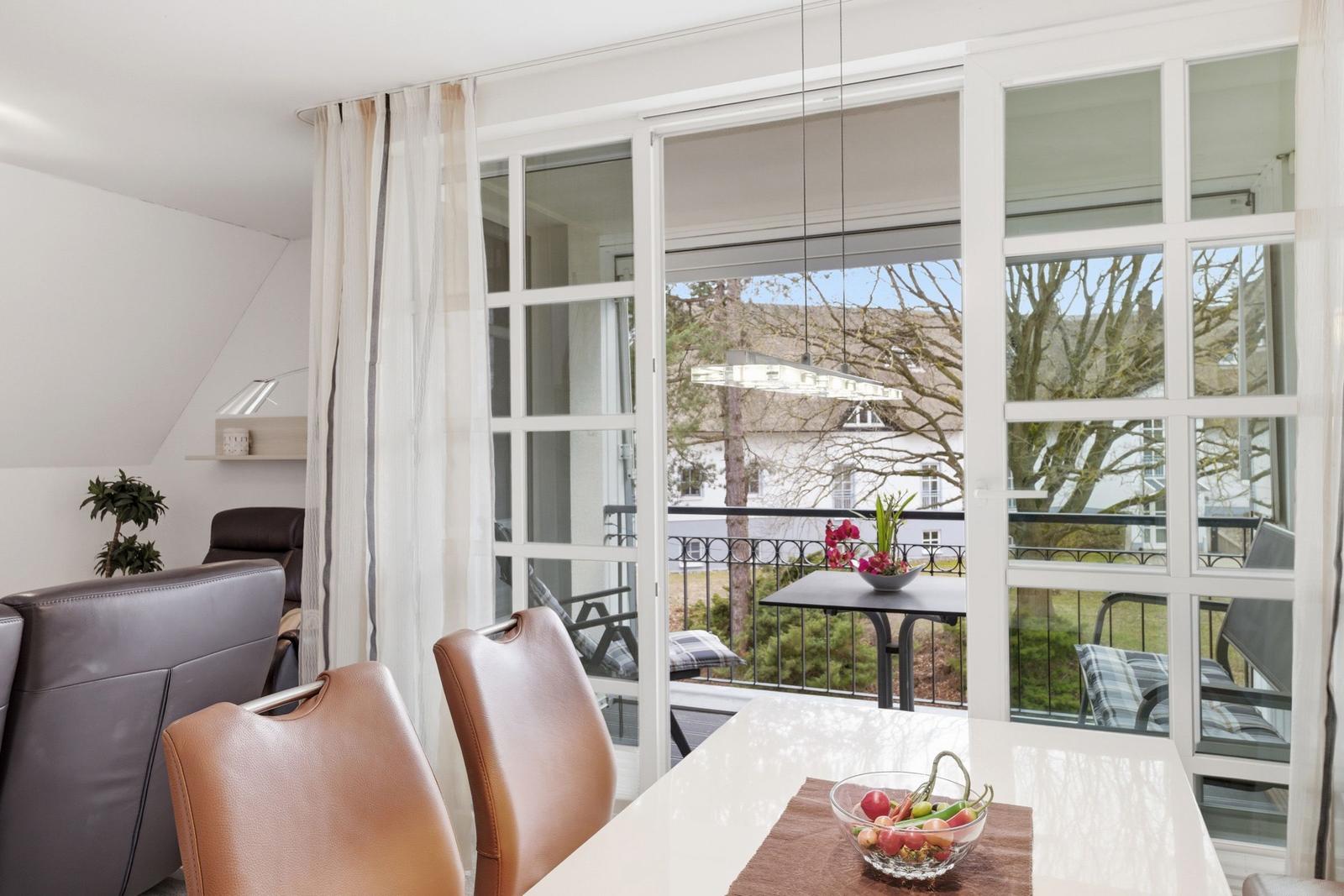 Dining area with view of balcony and garden. Table with fruit bowl and chairs.