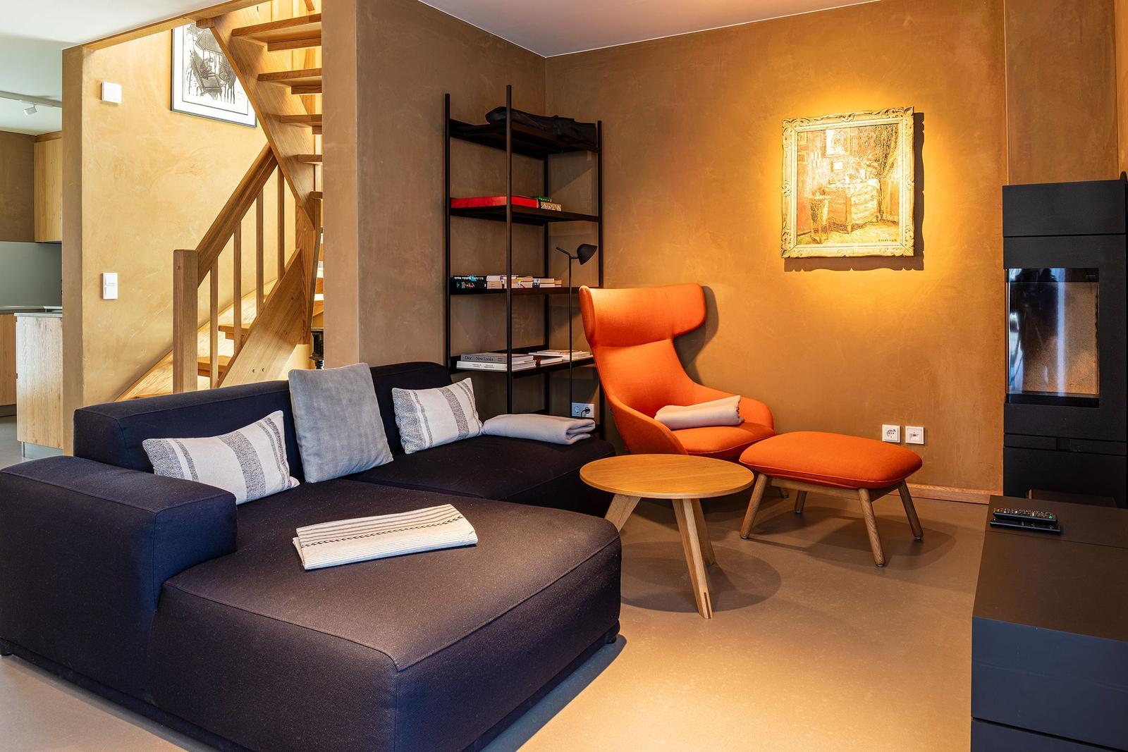 Ein Wohnzimmer mit Sofa, orange Sessel, Bücherregal und Kamin.
