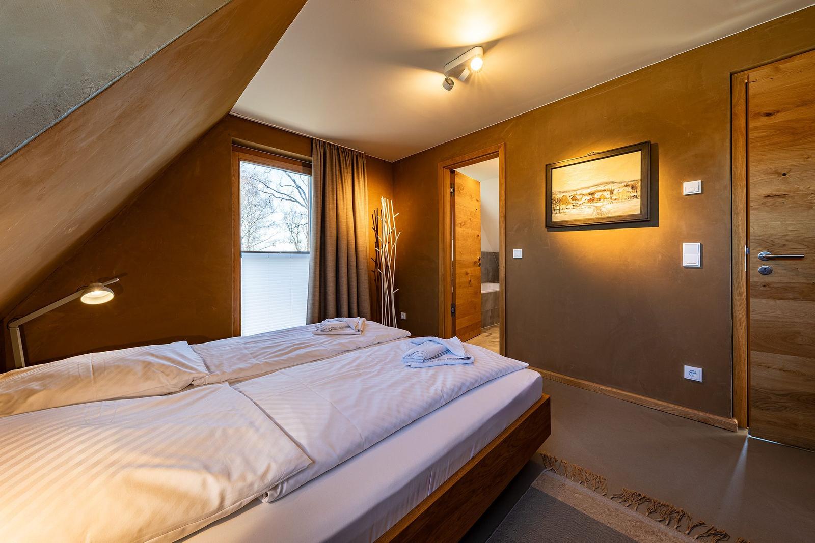 Schlafzimmer mit Doppelbett, Fenster und Tür zum Bad.