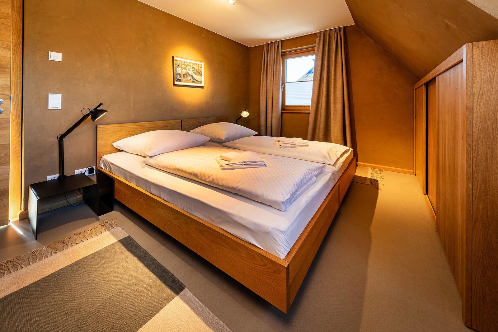 Schlafzimmer mit Doppelbett, Holzmöbel und Fenster mit Vorhängen.