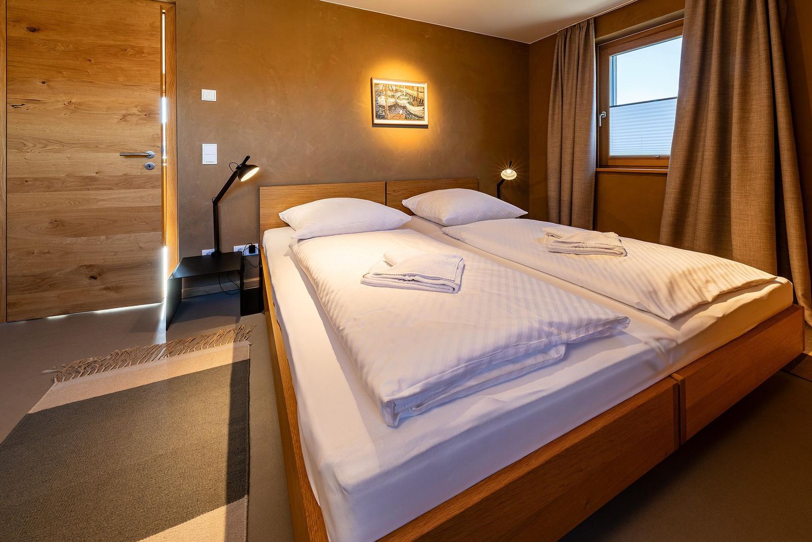 Ein Schlafzimmer mit einem Doppelbett, Holzwand und Fenster mit Vorhängen.
