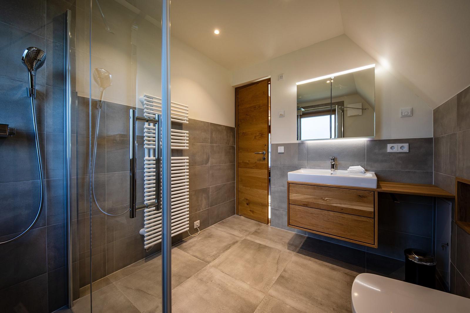 Badezimmer mit Dusche, Waschtisch und Toilette. Holz- und Steinoptik.