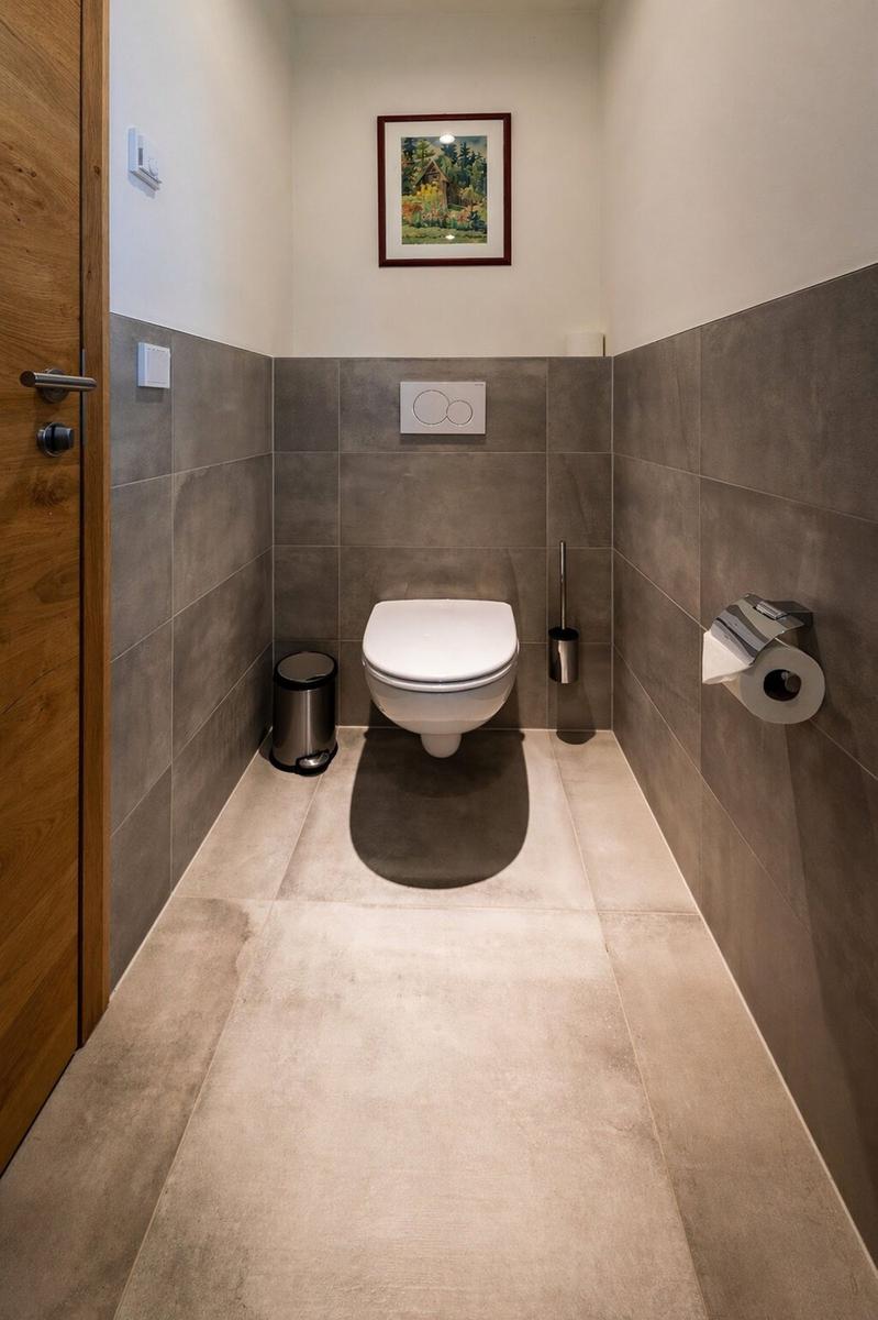 Toilettenraum mit Wandfliesen, Toilette, Toilettenpapierhalter und Bild an der Wand.