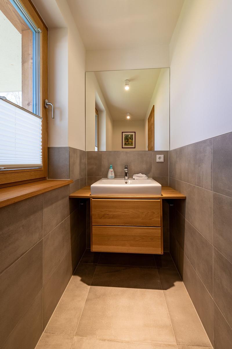Badezimmer mit Waschbecken, Spiegel und Fenster mit Jalousie.
