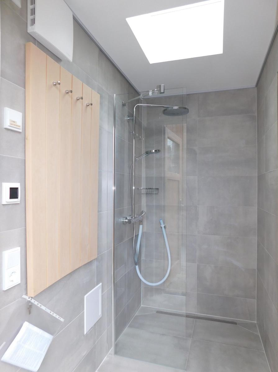 Dusche mit Glaswand, Holzregal und Dachfenster. Graue Fliesen und moderne Ausstattung.