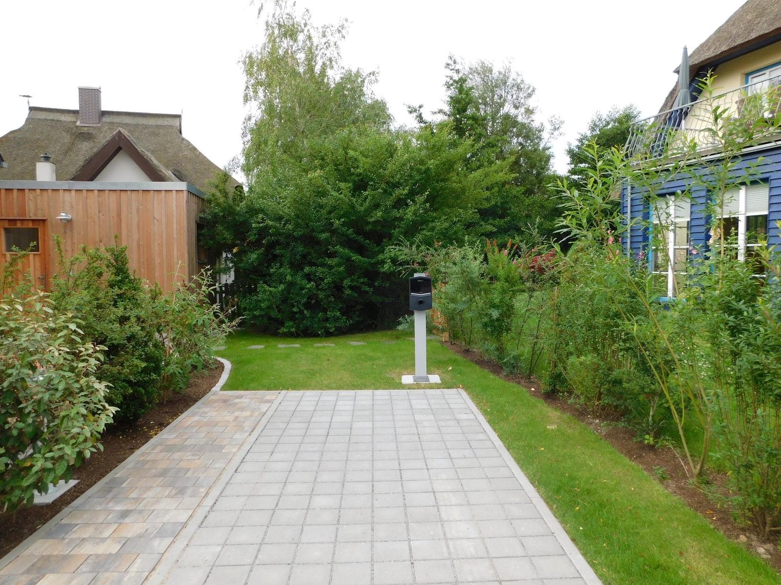 Pflasterweg führt durch grünen Garten zu einem Haus mit Dach und Terrasse.