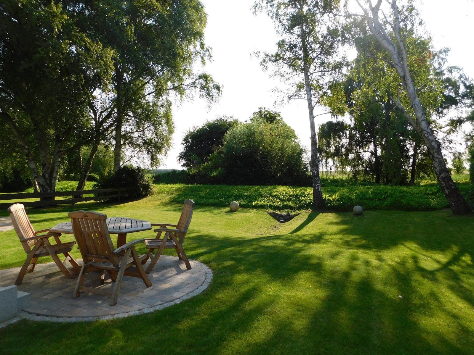Terrasse mit Holztisch und Stühlen im Garten unter Bäumen.