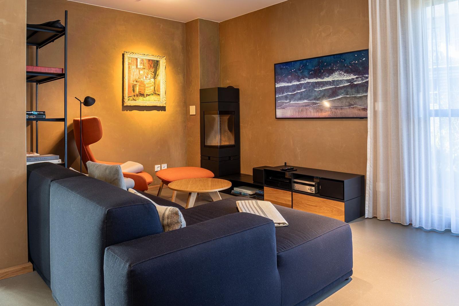 Wohnzimmer mit Sofa, Kamin, Wandbild und Fenster mit Vorhängen.