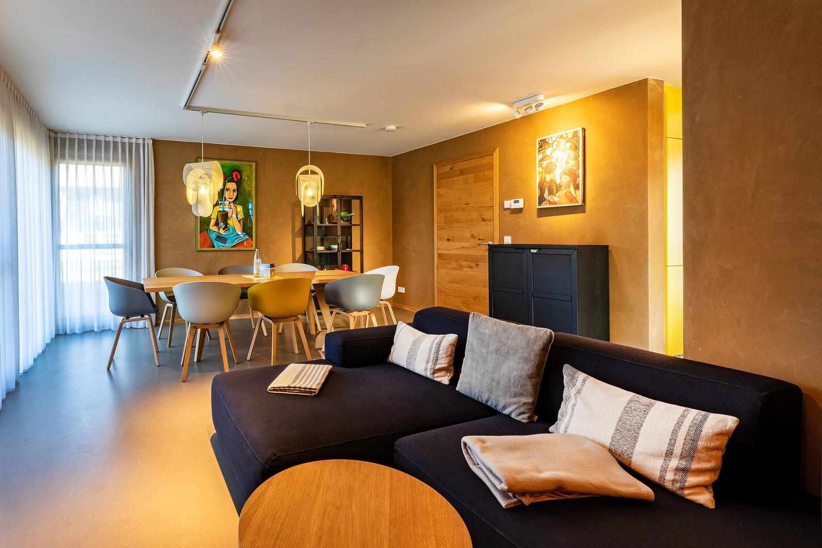 Wohn- und Essbereich mit Sofa, Tisch und Stühlen. Wandbild und Beleuchtung sichtbar.