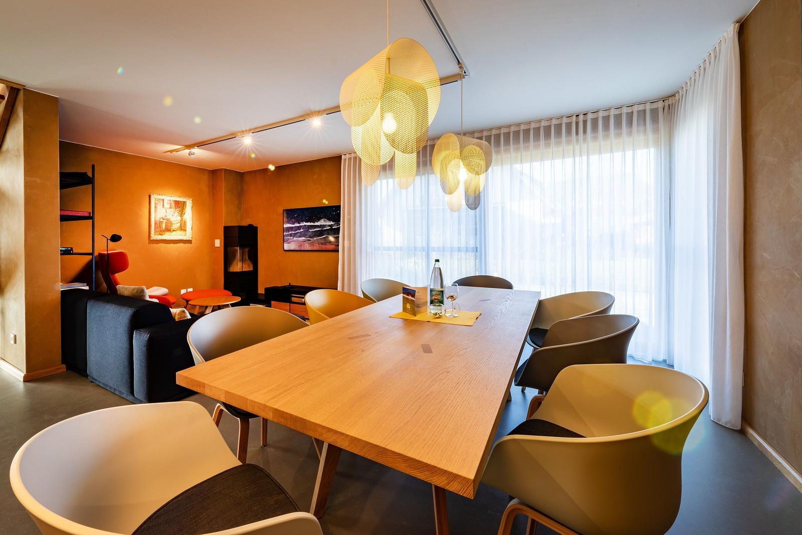 Esszimmer mit Holztisch, modernen Stühlen und großen Fenstern mit weißen Vorhängen.