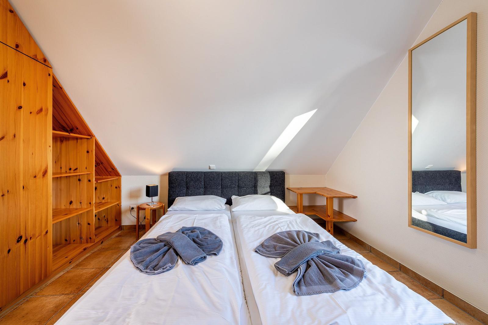 Zimmer mit Doppelbett, Holzmöbel und Dachschrägen. Spiegel und Nachttisch sichtbar.