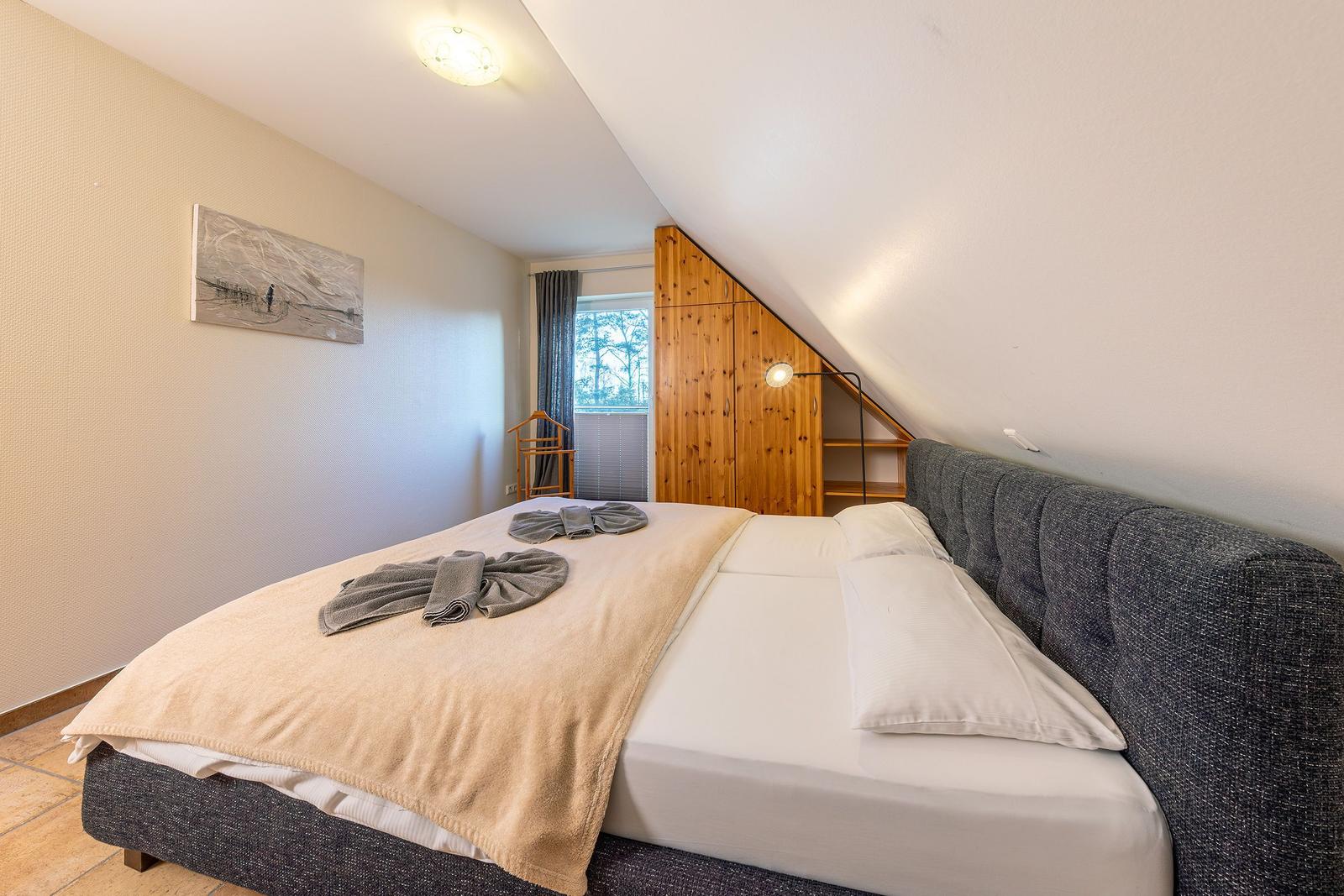 Schlafzimmer mit Doppelbett, Holzschrank und Fenster mit Blick auf Bäume.