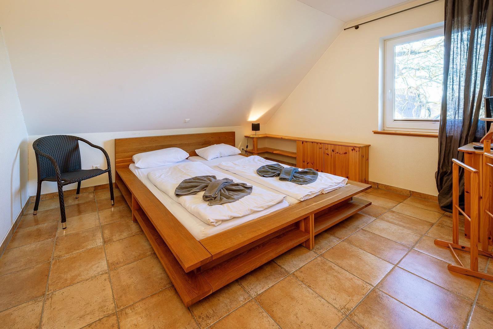 Schlafzimmer mit Holzbett, Sitzgelegenheit und Fenster