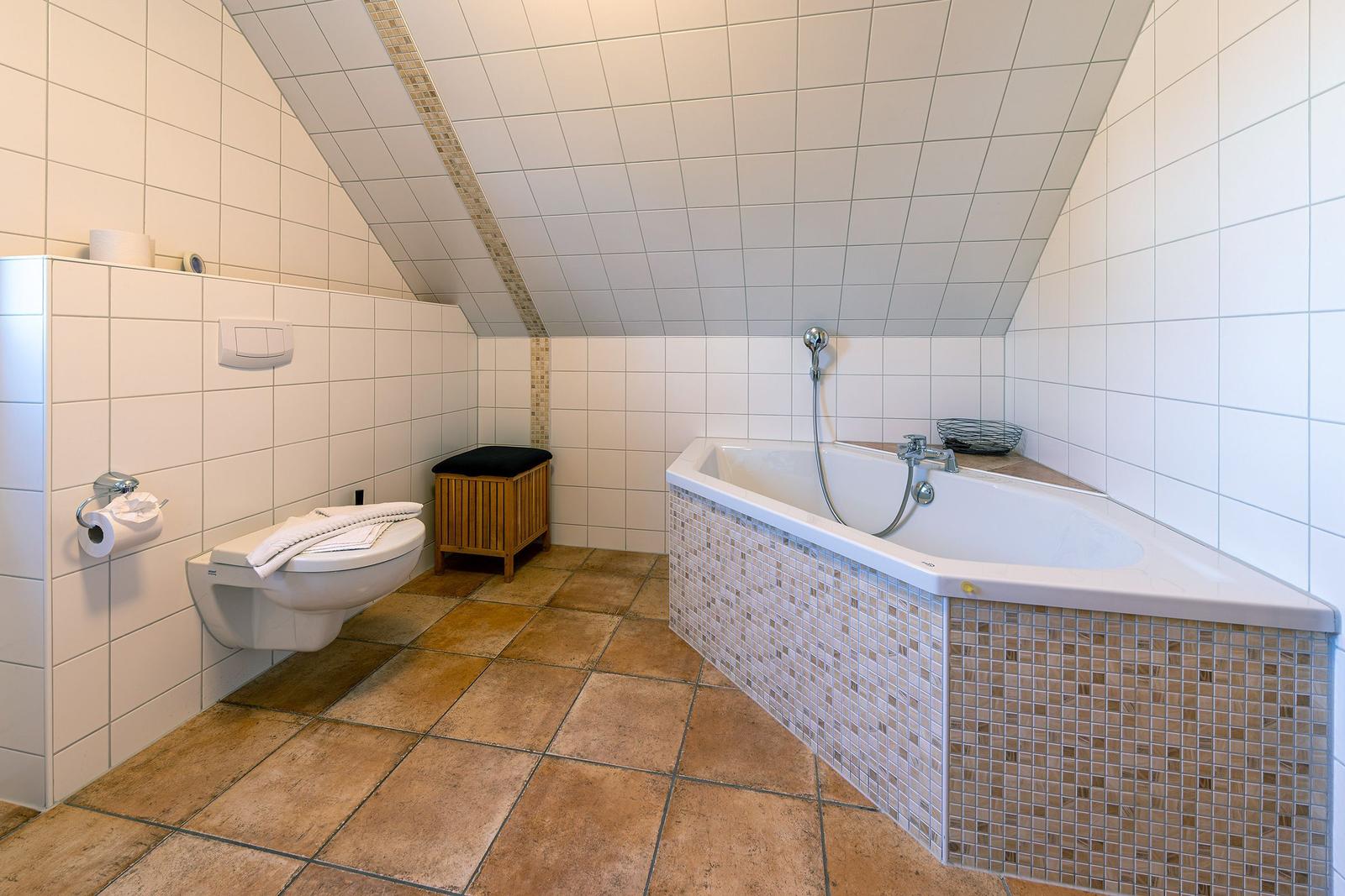 Dusche und Badewanne in einem Dachbodenbad mit weißen Fliesen und braunen Bodenfliesen.