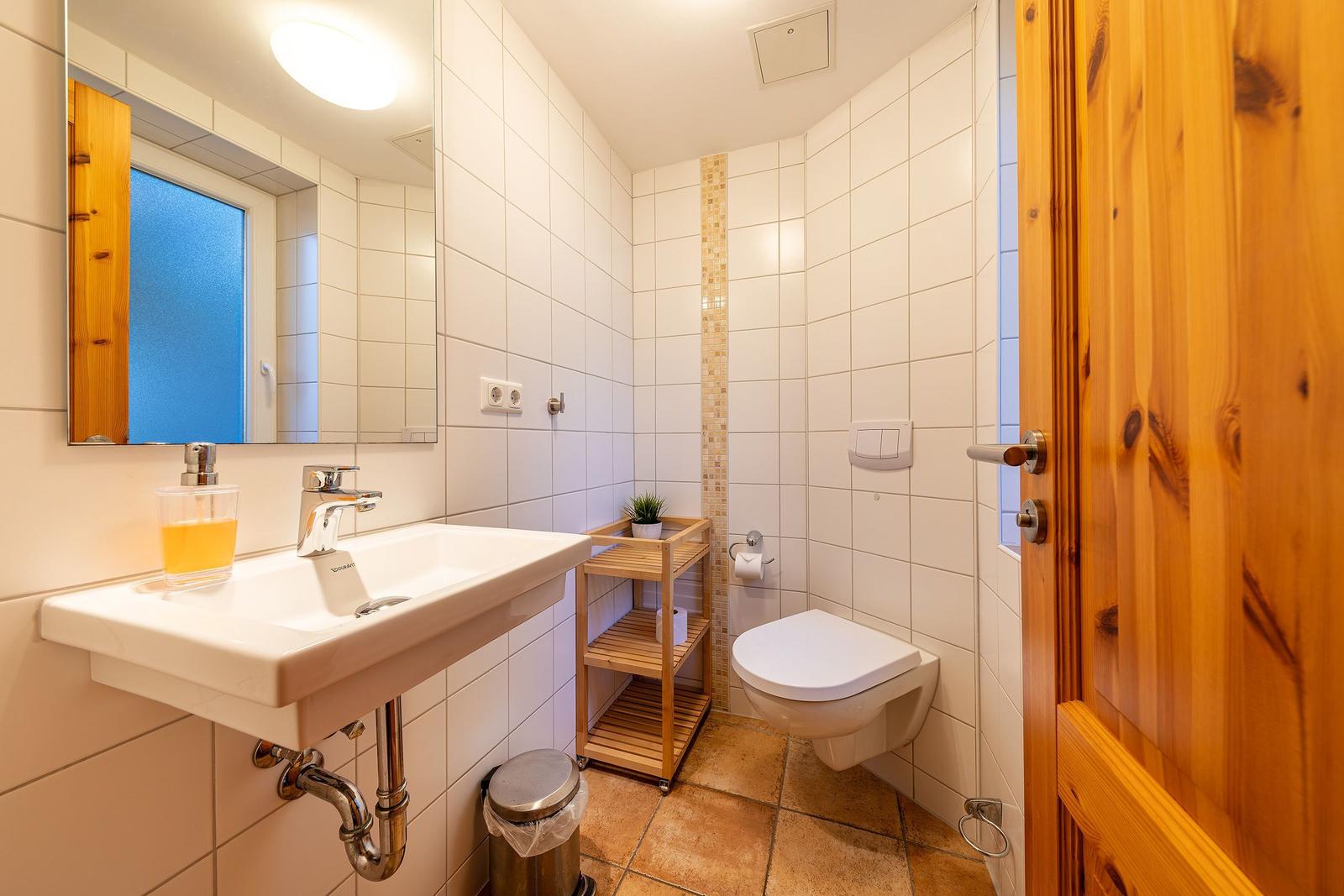 Badezimmer mit Waschbecken, Spiegel, Toilette und Holzregal.