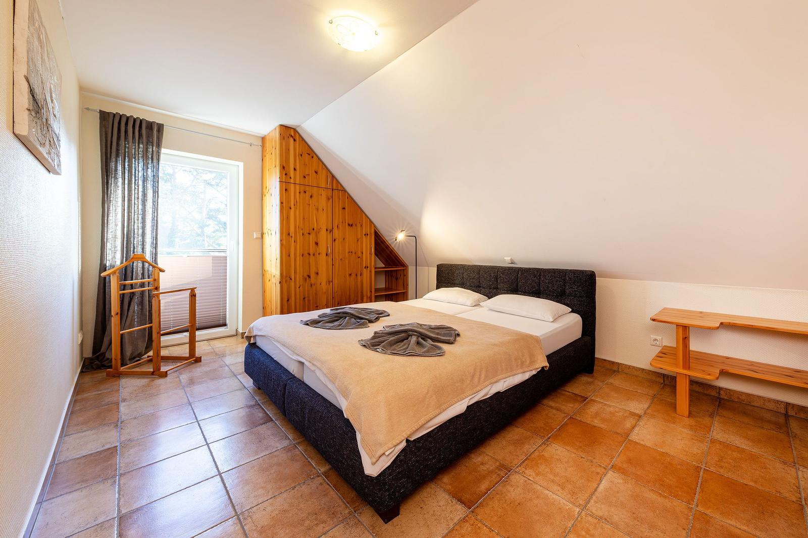 Schlafzimmer mit Doppelbett, Holzmöbel und Fenster mit Blick nach draußen.