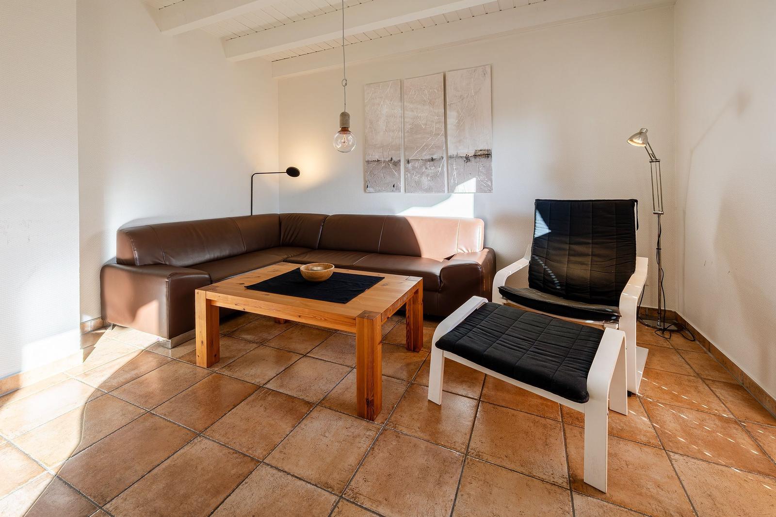 Wohnzimmer mit braunem Sofa, Holztisch und weißem Sessel auf Terrakottaboden.