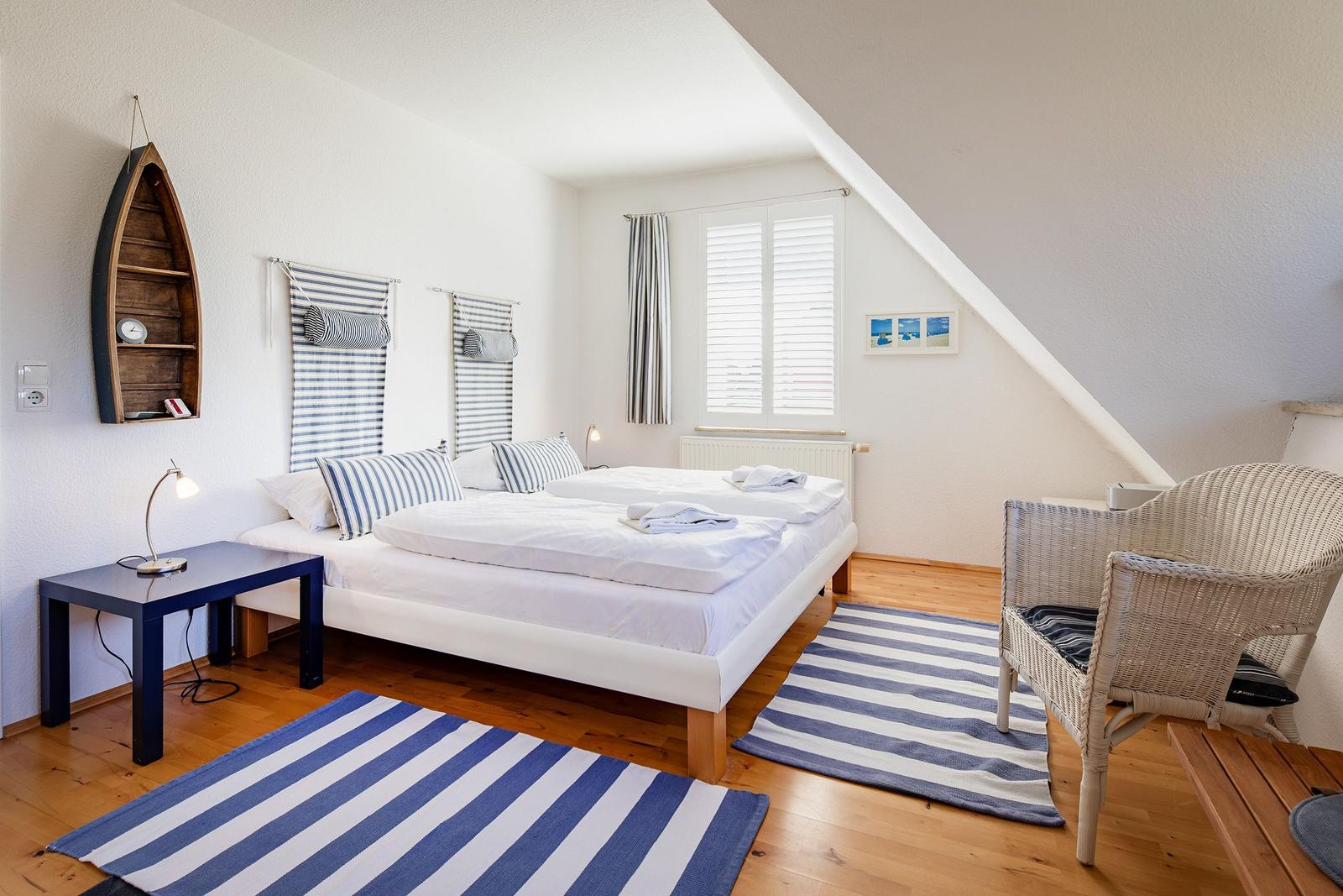 Schlafzimmer mit Doppelbett, Holzboden, gestreiften Teppichen und einem Hängeregalschiff.