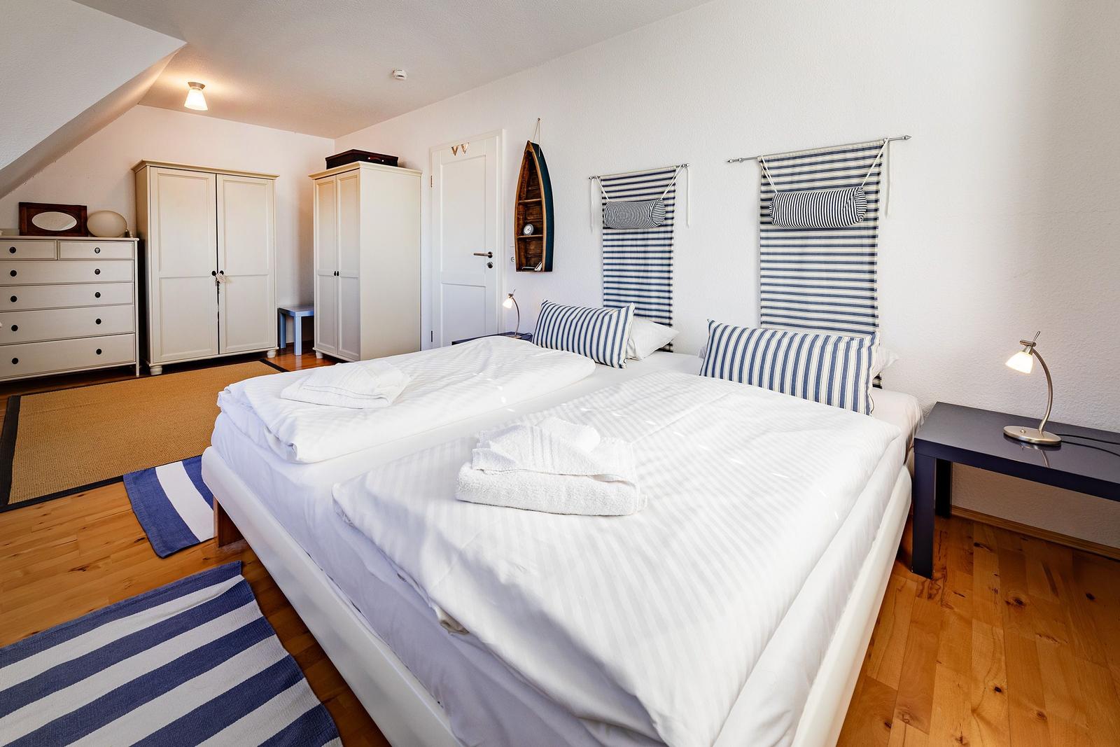Schlafzimmer mit Doppelbett, blau-weißen Streifen und Holzboden
