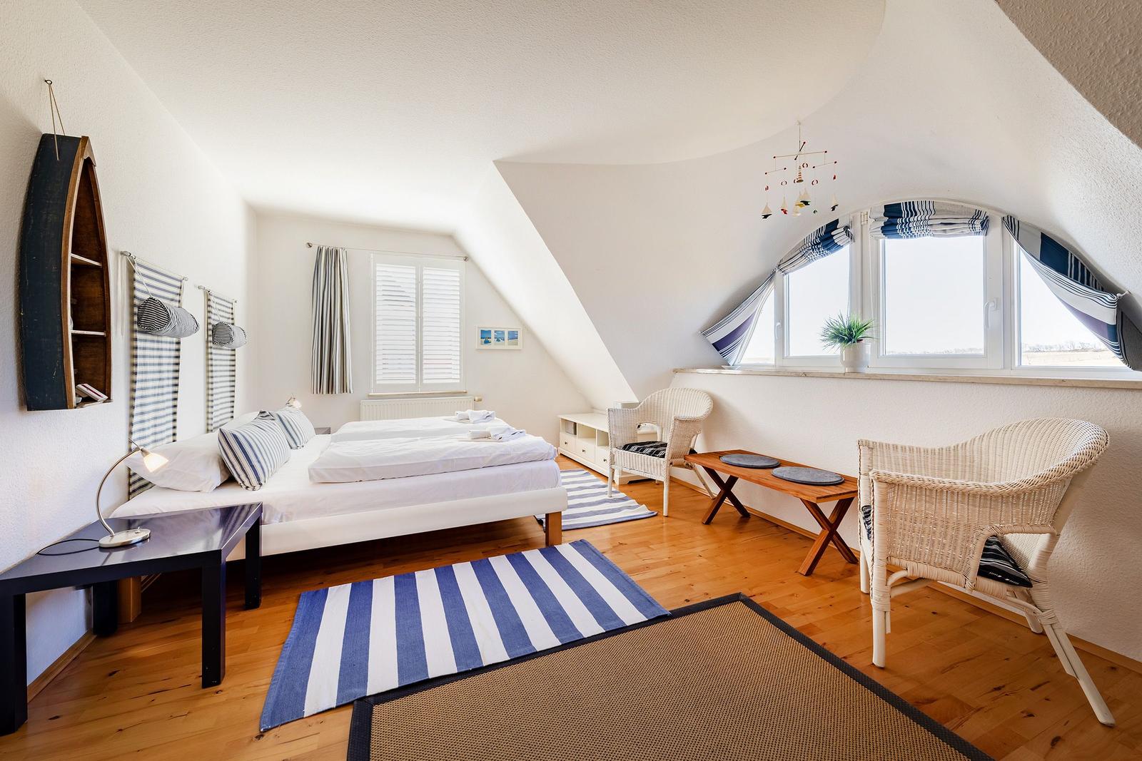 Schlafzimmer mit Dachschräge, Bett, zwei Stühlen und Fenster mit Blick.