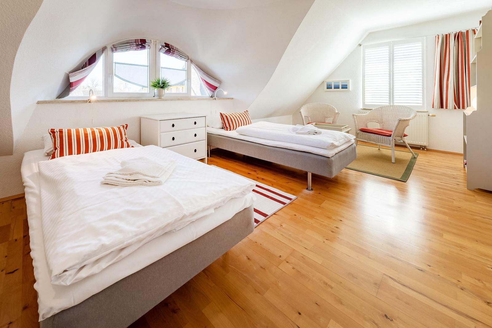 Zimmer mit zwei Betten, Holzboden und Fenstern mit Vorhängen.