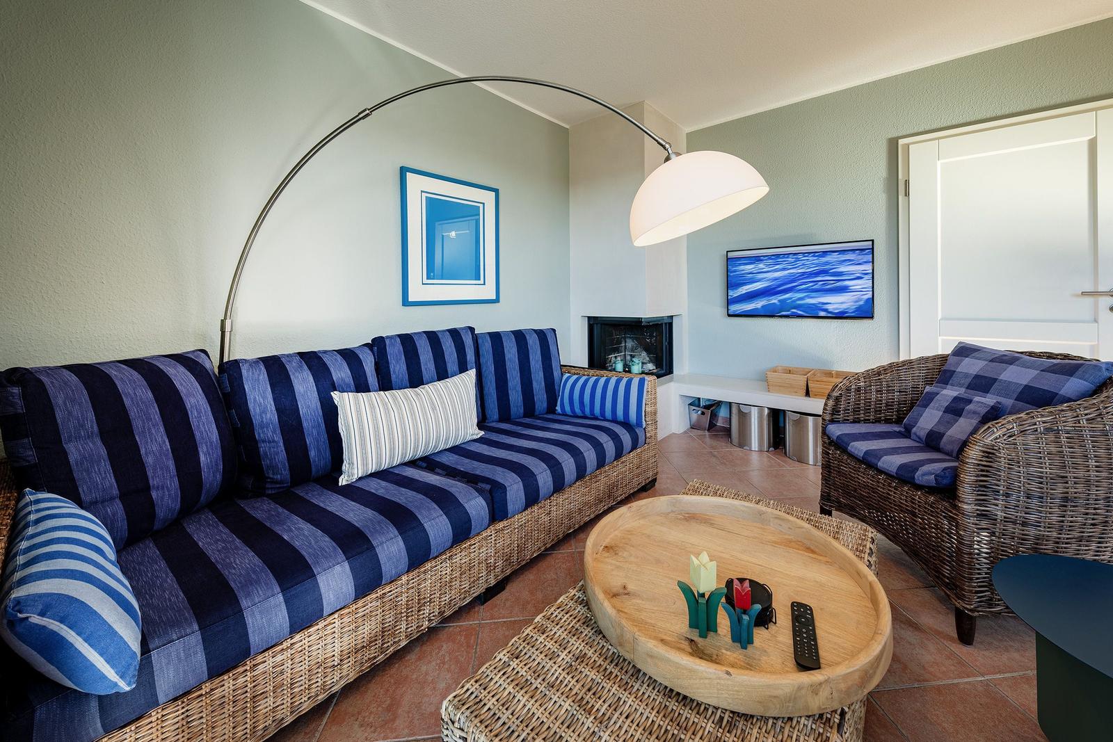 Wohnzimmer mit Sofa, Sessel und Fernseher. Holztisch und Stehlampe.