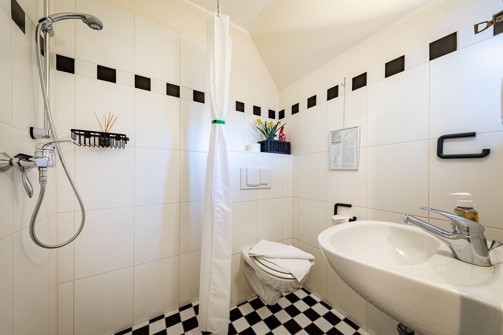 Badezimmer mit Dusche, Toilette und Waschbecken. Schwarze und weiße Fliesen.