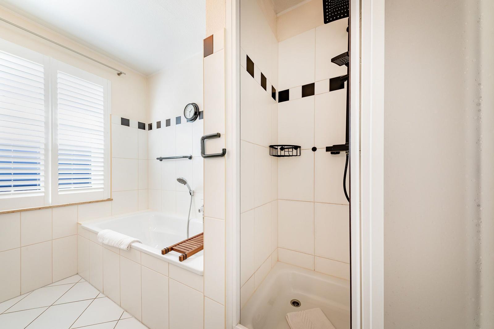 Bad mit Badewanne und Dusche, Fenster mit Jalousie, weiße Fliesen und Handtuch.