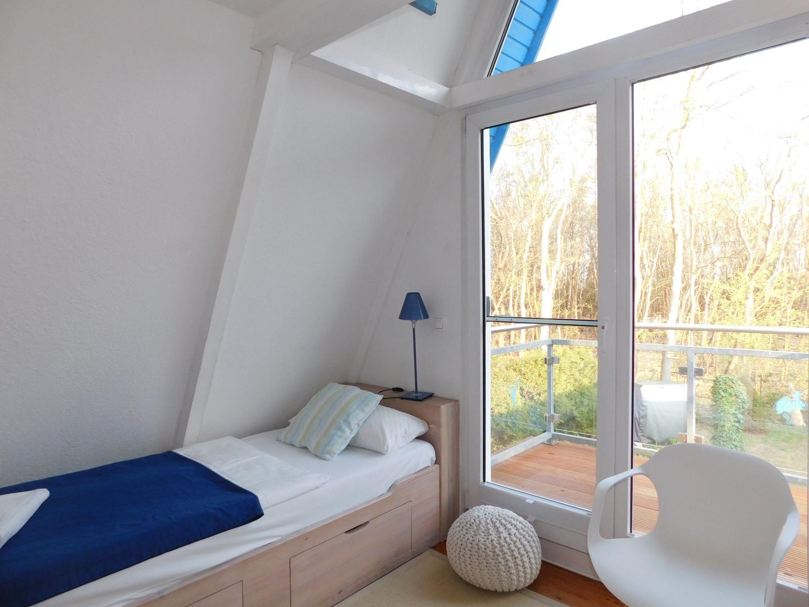Ein Schlafzimmer mit Dachschrägen, Bett, Stuhl und Balkon mit Blick in den Wald.