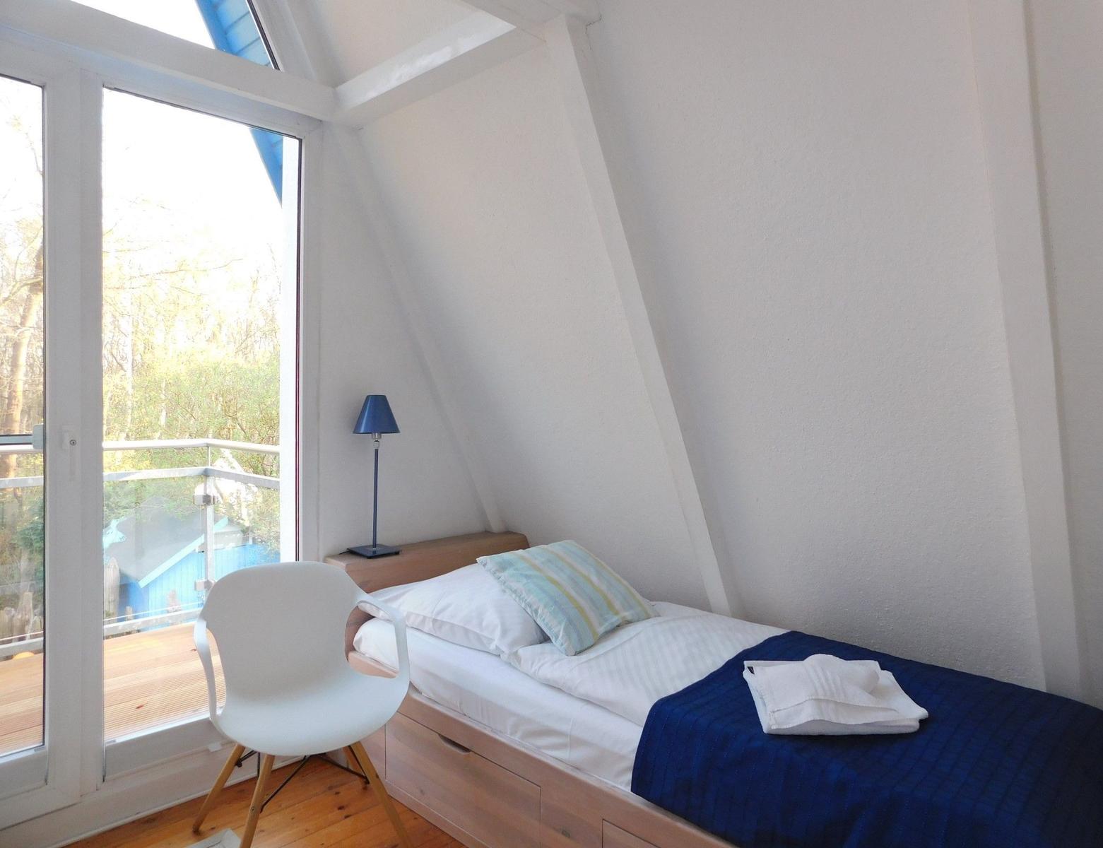 Ein Schlafzimmer mit Dachschrägen, Bett, Stuhl und Fenster zum Balkon.