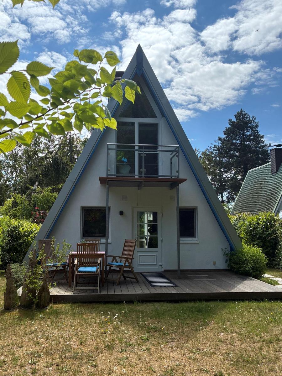 A-frame-Haus mit Balkon und Terrasse im Garten. Holztisch und Stühle.