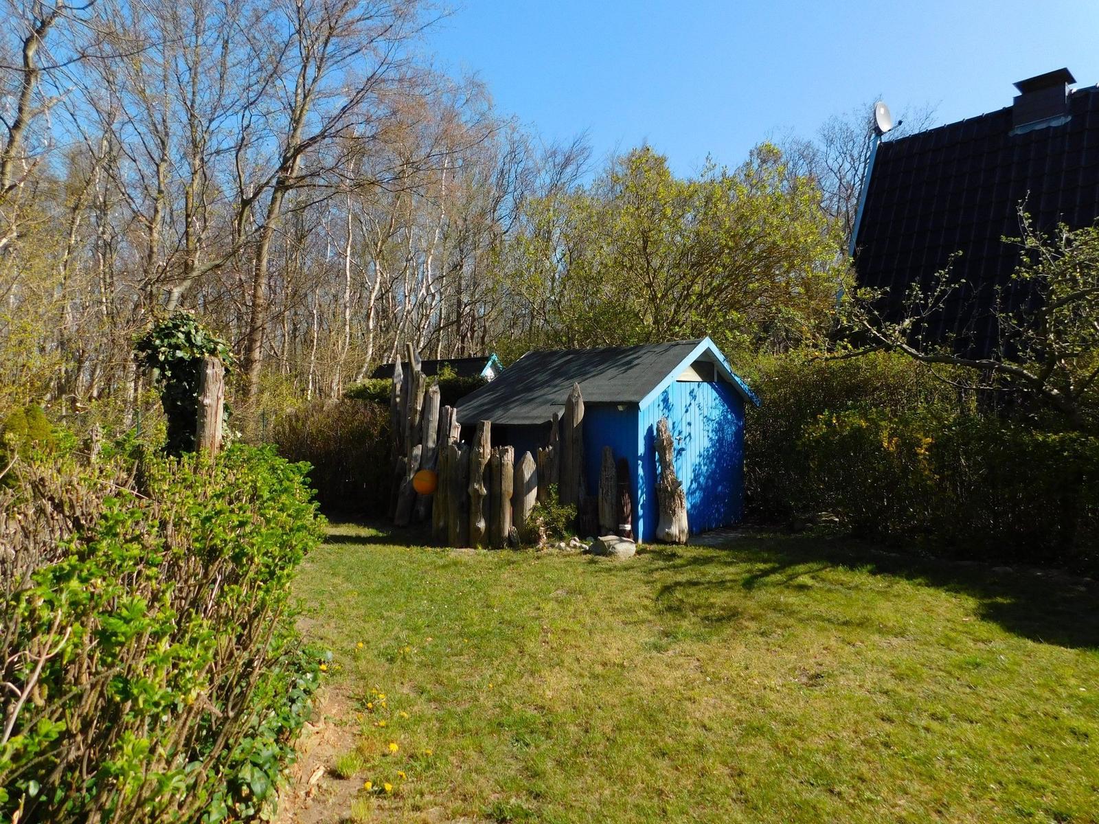 Ein blauer Schuppen mit Holzzaun steht auf einer Wiese neben einem Haus.