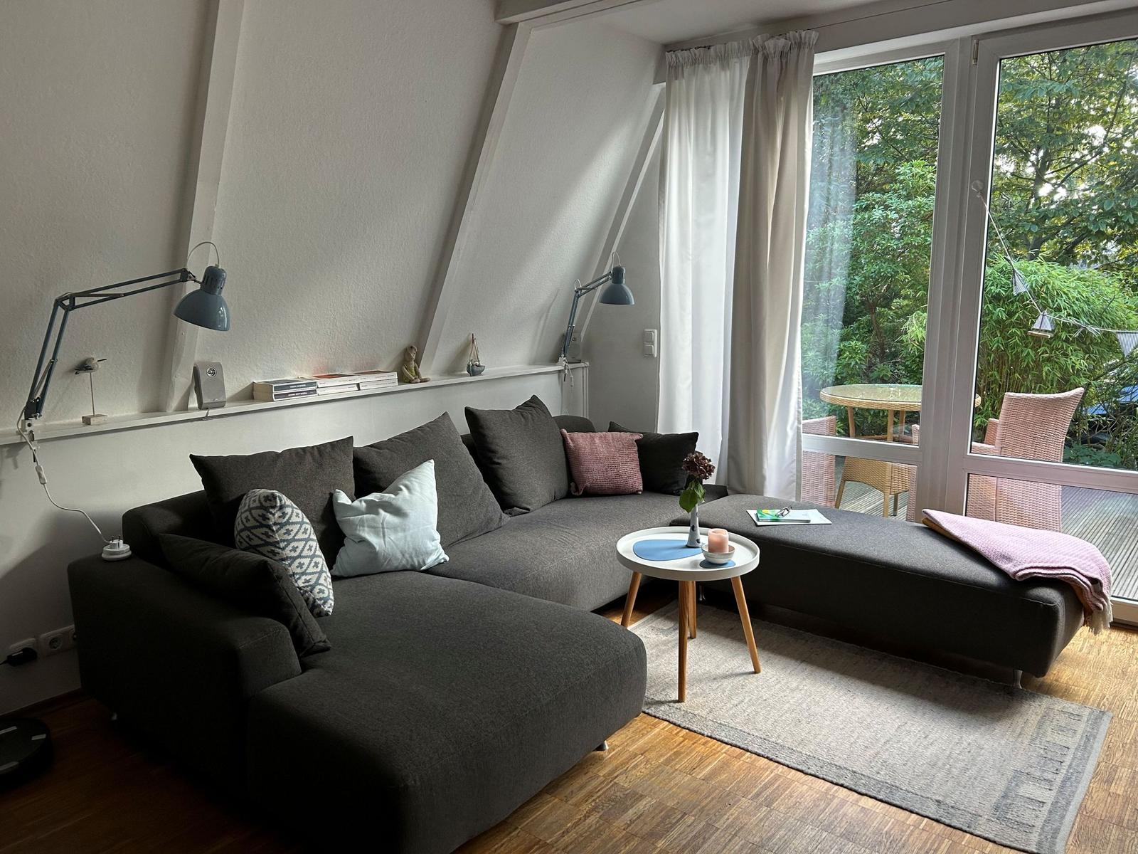 Ein Wohnzimmer mit grauem Sofa, Holzboden und Blick auf einen Garten.