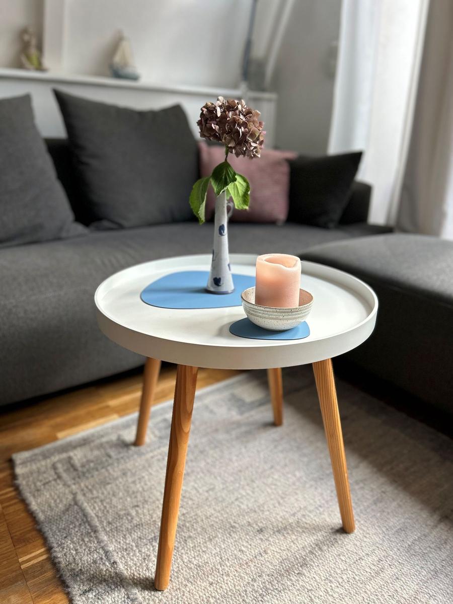 Runder Tisch mit Blumenvase und Kerze vor grauem Sofa