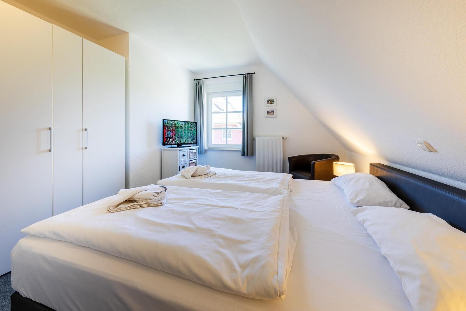Schlafzimmer mit Doppelbett, Kleiderschrank, Fernseher und Fenster.